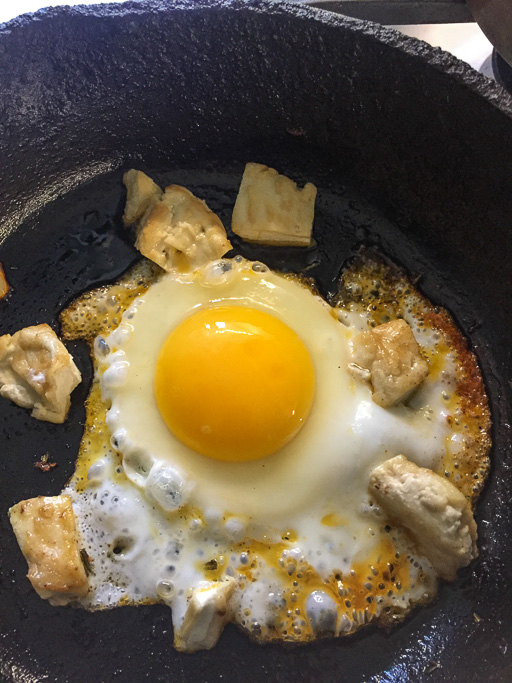 Photo of a sunny-side-up egg being fried with mushroom pieces
